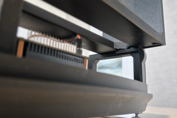 Low-angle close-up of the join between the black base and drive rails, showing a printed snap-fit tab above the Pi's pin header.