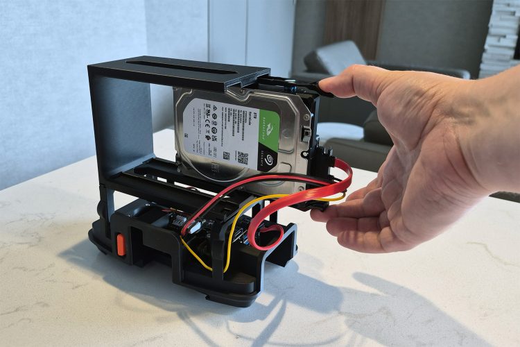 A hand sliding an 8 TB Seagate BarraCuda drive in its HP caddy sideways out of the open chassis, with red SATA and power cables trailing to the board below.