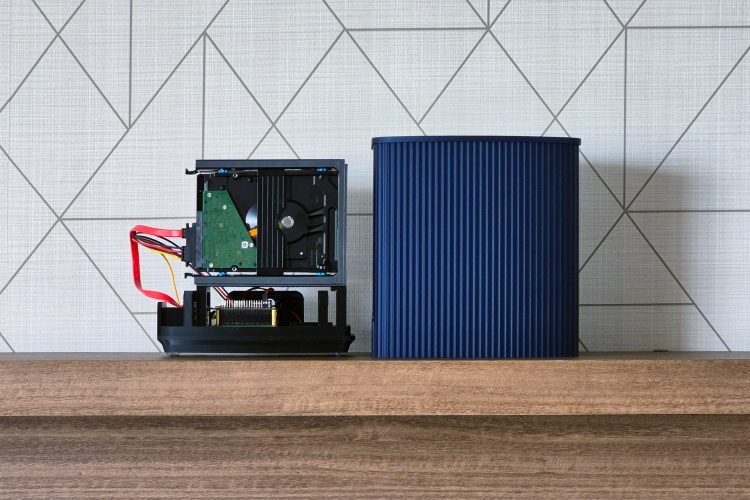 Front view of the open black chassis with an 8 TB drive in its caddy and red SATA cable, beside the blue ridged shroud standing on the same shelf.
