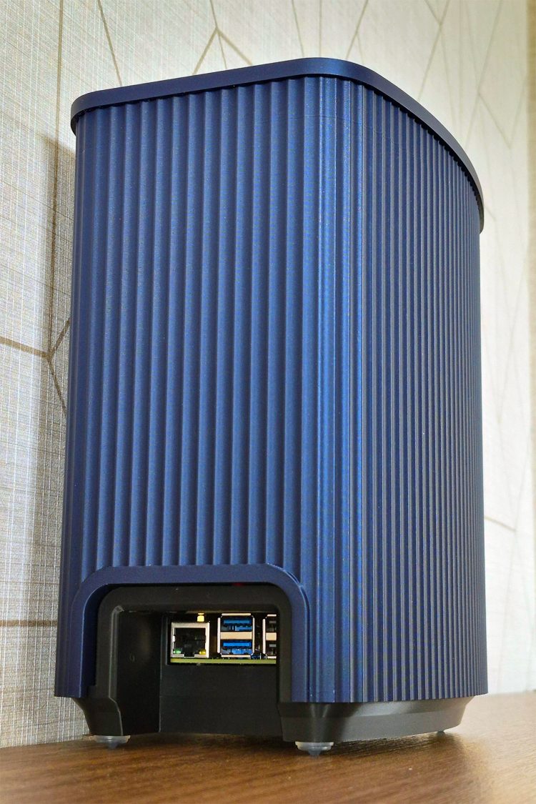 Angled view of the blue ridged enclosure with a base cut-out exposing the Pi 5's Ethernet and USB ports above small rubber feet.